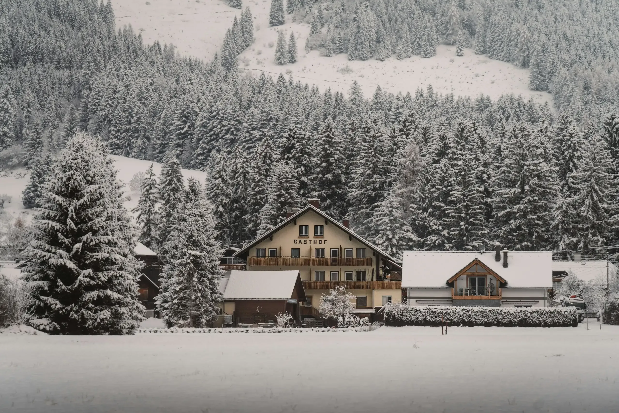 Un gasthof de munte cu balcoane de lemn, între brazi acoperiți de zăpadă